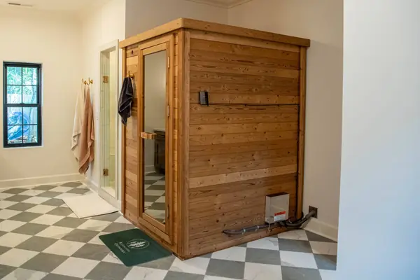 Cedar sauna built into the corner of the primary bath, over checkerboard tile