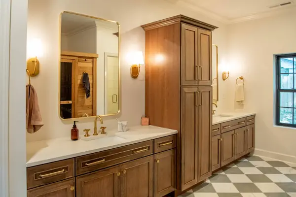 Double vanity with stained wood cabinetry, brass fixtures and a linen tower